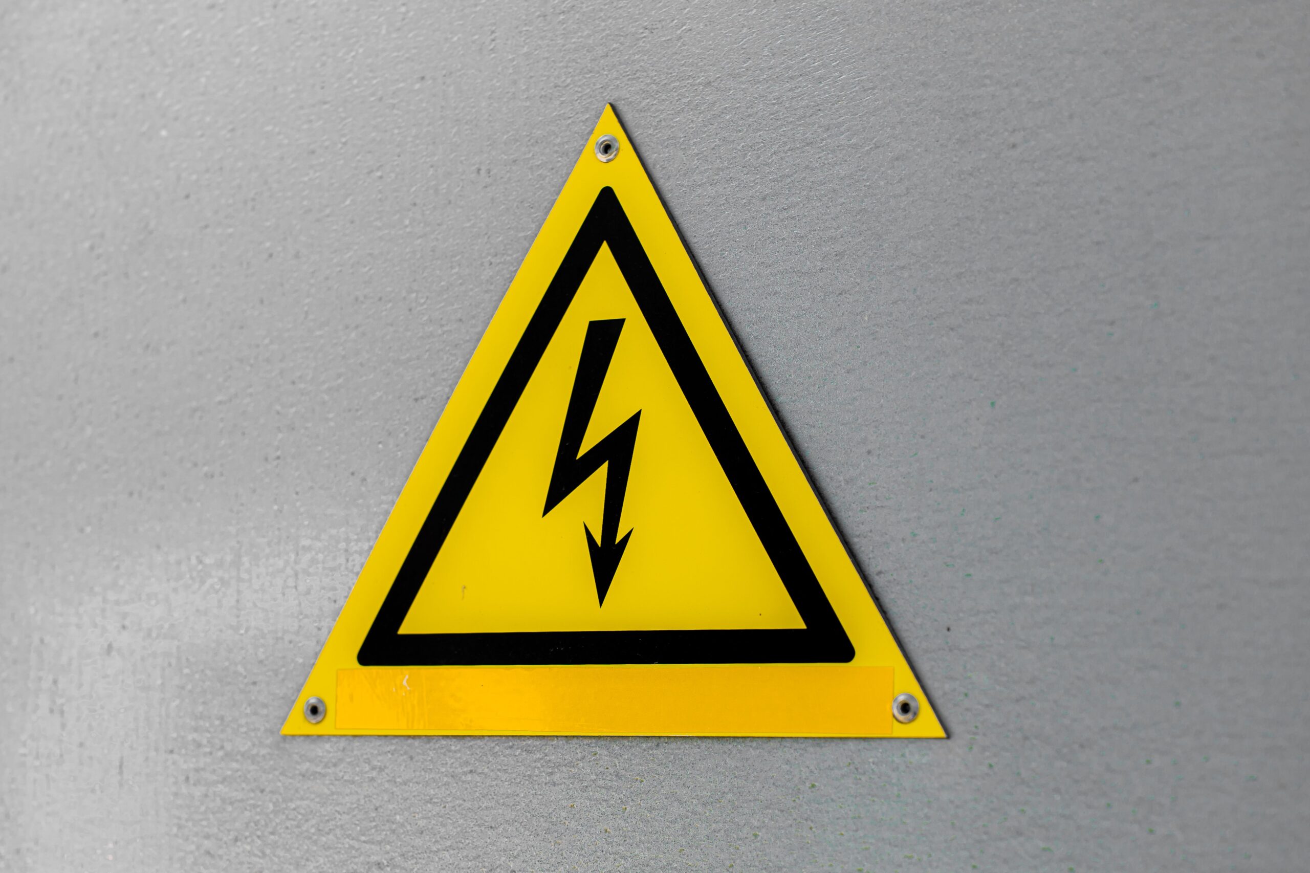 Close-up of a yellow high voltage warning sign mounted on a wall.